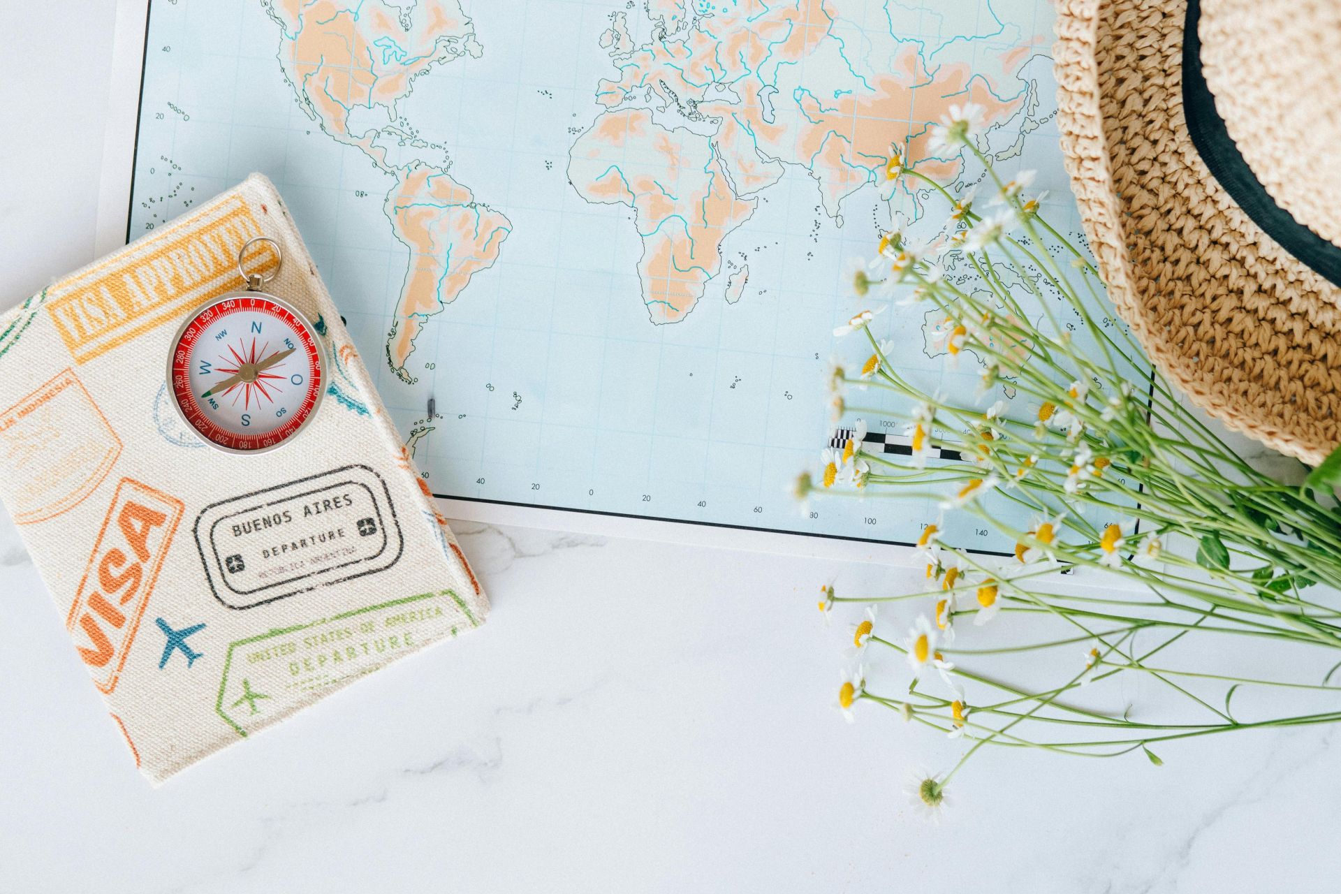 Flat lay of world map, compass, passport, and chamomile flowers, perfect for travel enthusiasts.